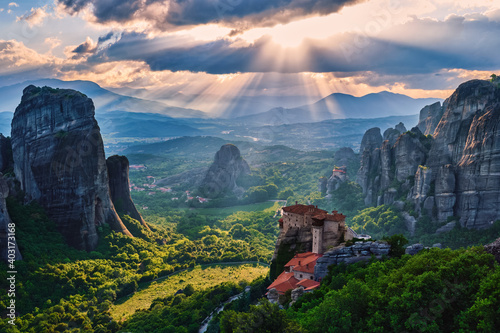 Sunset view of nunnery of Moni Agias Varvaras Roussanou and rocks of Meteora, Greece and valley. Cloudy sky, sun rays fall upon. UNESCO World Heritage