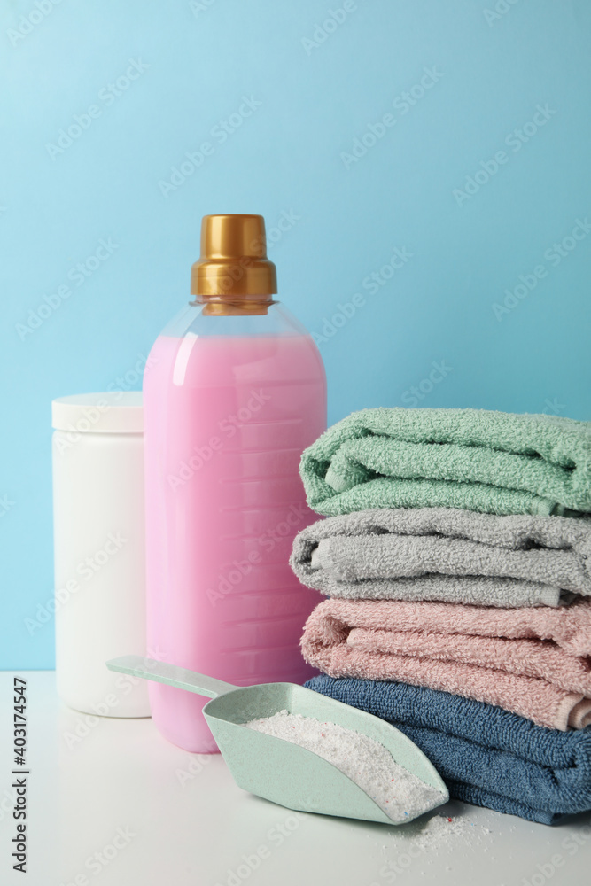 Detergent, scoop with powder and towels on white table against blue background Detergent, scoop with powder and towels on white table against blue background