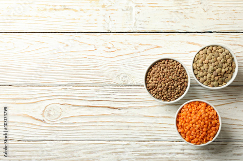 Bowls with different legumes on wooden background, space for text