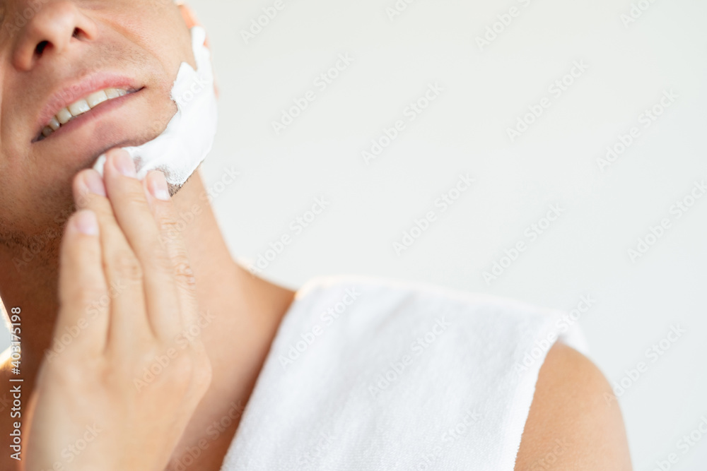 Male grooming. Barber shop. Cosmetic product. Skincare treatment. Cropped portrait of satisfied man applying white shaving foam on face chin with hand isolated on neutral background.