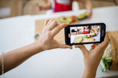 Female hands with a smartphone recording a little girl cutting an avocado