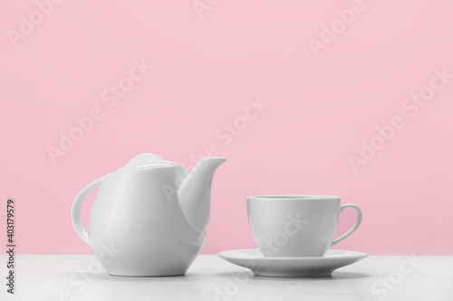 Teapot and cup on table against color background
