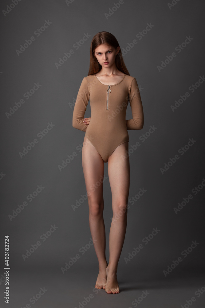 beautiful girl in nude bodysuit posing barefoot in the studio on a gray background
