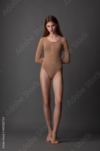 beautiful girl in nude bodysuit posing barefoot in the studio on a gray background