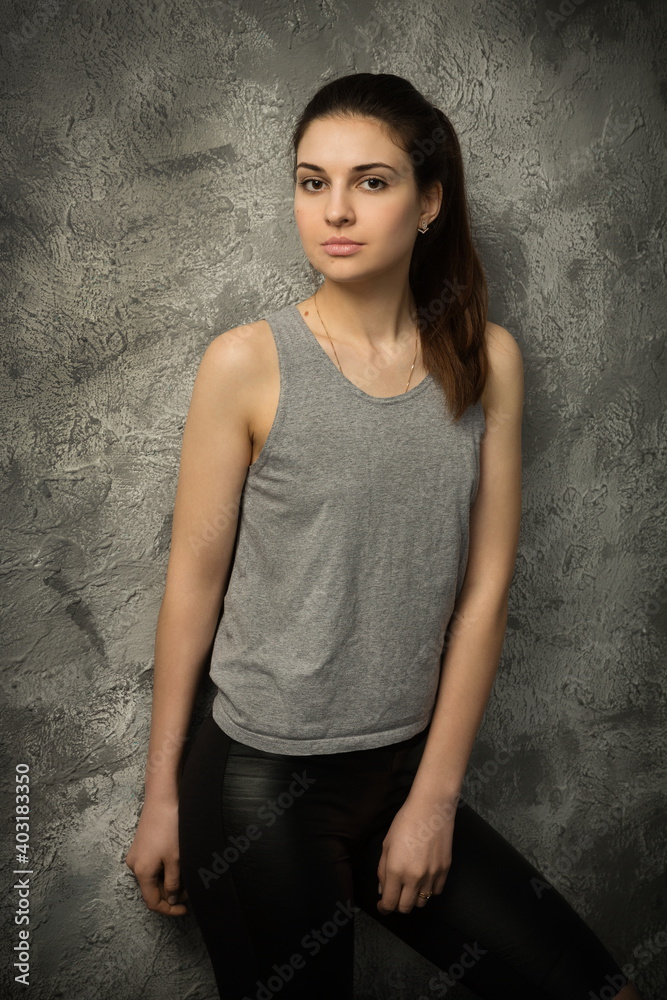 beautiful sexy girl in a gray tank top and black pants posing against the background of an old cracked wall beautiful sexy girl in a gray tank top and black pants posing against the background of an old cracked wall