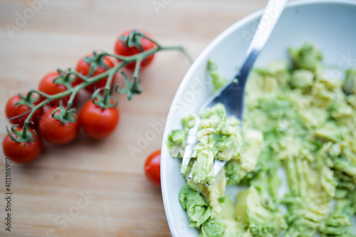 Cherry tomatoes and bowl of mashed avocado on wooden table