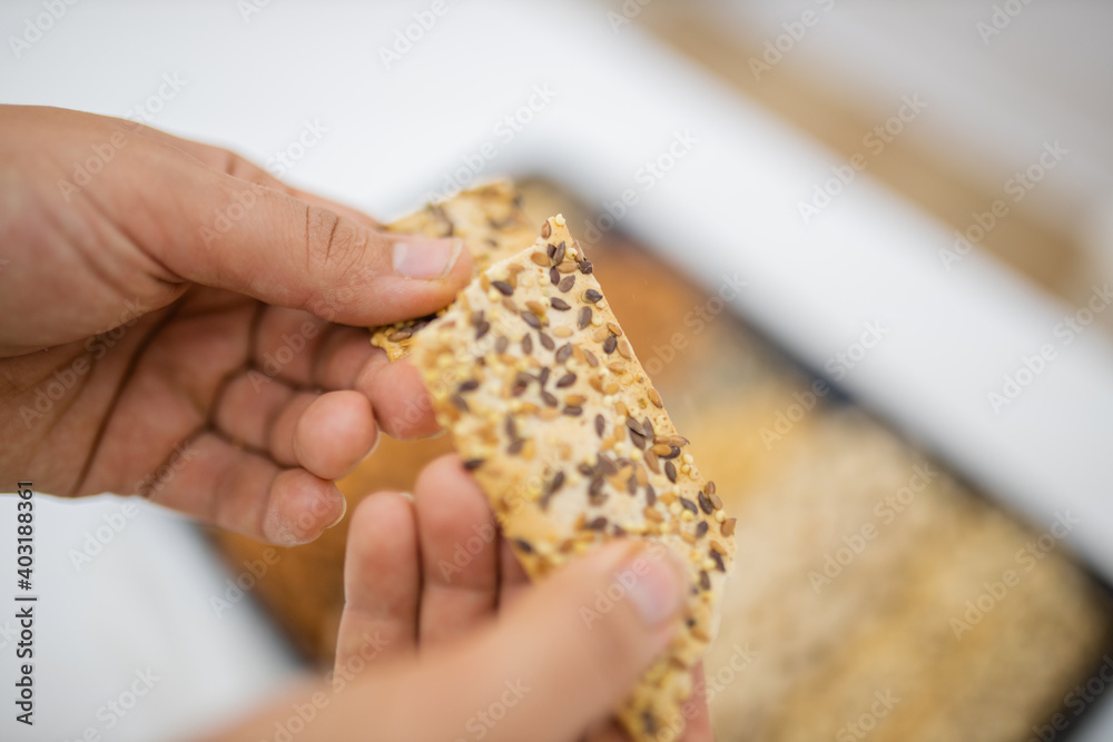 Female hand holding multi-seed crispbread above a tray with seeds and nuts Female hand holding multi-seed crispbread above a tray with seeds and nuts