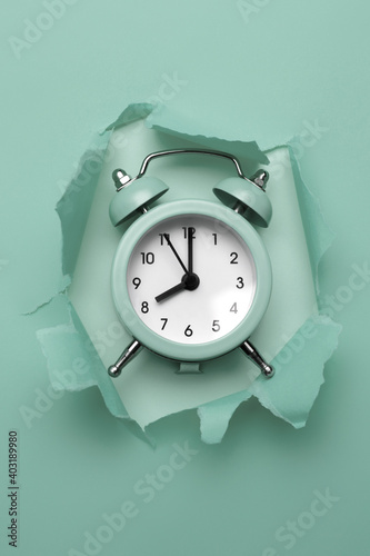 Classic round alarm clock in the paper hole with torn sides. Through paper. Ripped hole. Deadline concept. photo