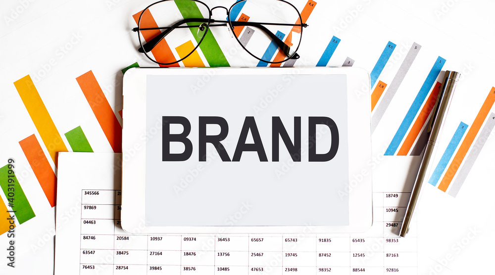 The tablet with text BRAND on business charts and pen The tablet with text BRAND on business charts and pen