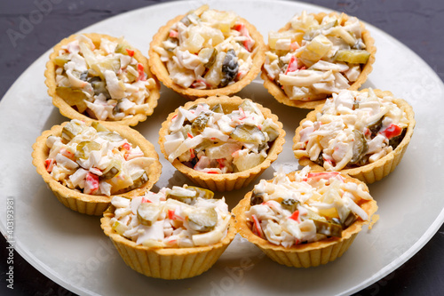 Tartlets with salad on a white plate on a dark background.