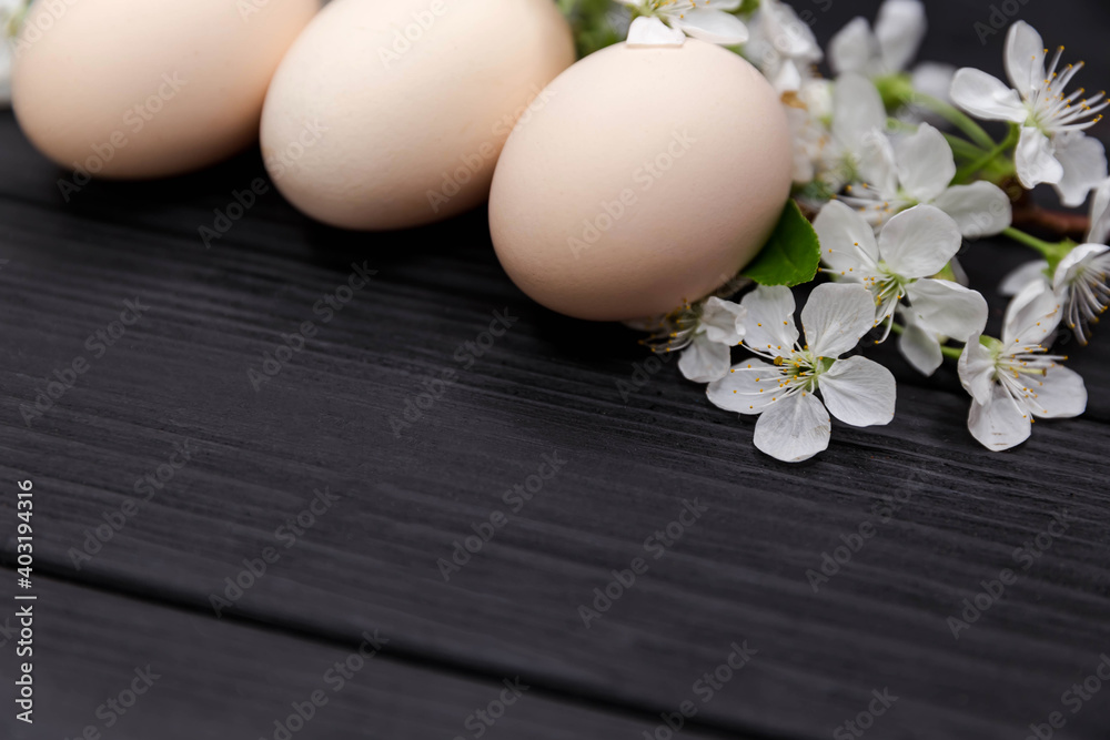 Uncolored natural easter eggs on black wooden background. Happy easter concept with white spring flowers. Composition of blooming tree branches. Easter card. Natural floral spring decorations