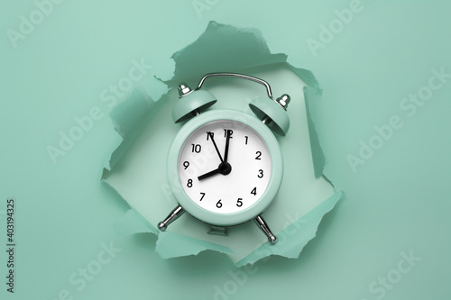 Classic round alarm clock in the paper hole with torn sides. Through paper. Ripped hole. Deadline concept.