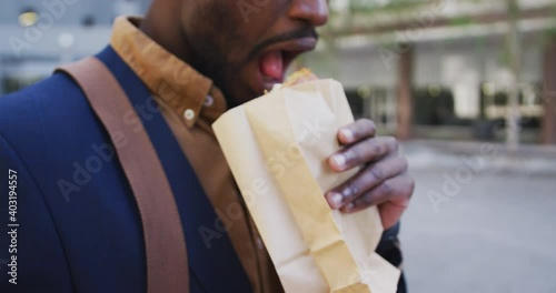 African american businessman eating sandwich in city street photo