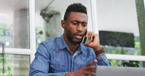 African american businessman talking on smartphone and using laptop outisde cafe cmmunication, busin photo