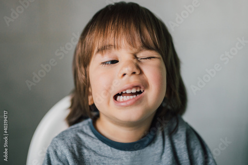 Portrait of adorable 3 year old kid learning to wink his eye. Cute caucasian boy with funny face expression. Real child having fun indoors with family. Healthy and happy childhood. Parenting concept. © Andra