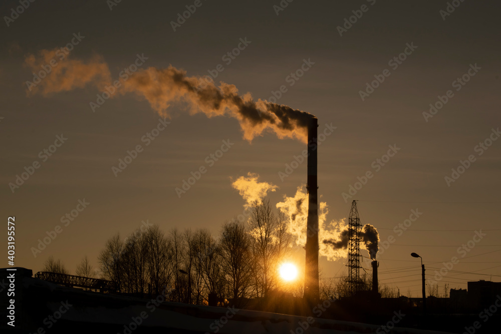 The chimney smokes against the rising sun in winter.