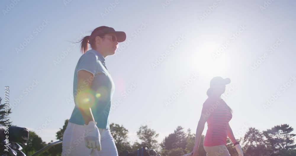 Two female caucasian golf players walking with their golf kit carts on the golf course