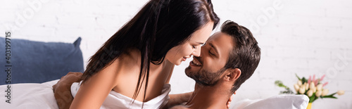 happy young man hugging brunette woman in bedroom on blurred background, banner