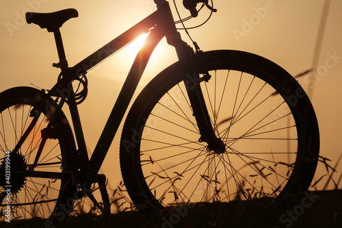 Silhouette of a bike at sunset. The sun shines through the bicycle frame at the field