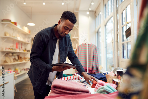 Male Small Business Owner Checks Stock In Shop Using Digital Tablet photo