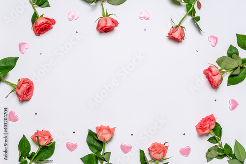 Frame made of fresh pink roses and hearts on white background. Beautiful floral greeting card for Valentine's, women's or mother's day. Mock up, flat lay, top view, copy space
