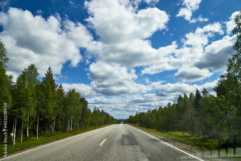 View from relief car windscreen on the blue sky with white clouds, grey asphalt road and landscape with forest and green teeses. Landscape through window View from relief car windscreen on the blue sky with white clouds, grey asphalt road and landscape with forest and green teeses. Landscape through window