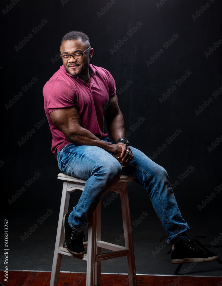 Handsome afro-american man sitting on high bar chair. Black background. Shirtless male model in pink shirt. Handsome afro-american man sitting on high bar chair. Black background. Shirtless male model in pink shirt.
