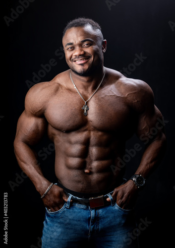 African american bodybuilder stands with hands in pockets on black studio background. Strong body.