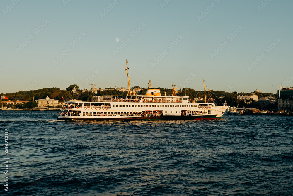 Tourist ship sails on the Golden Horn, scenic sunny beautiful waterfront  of Istanbul city at sunset in summer.