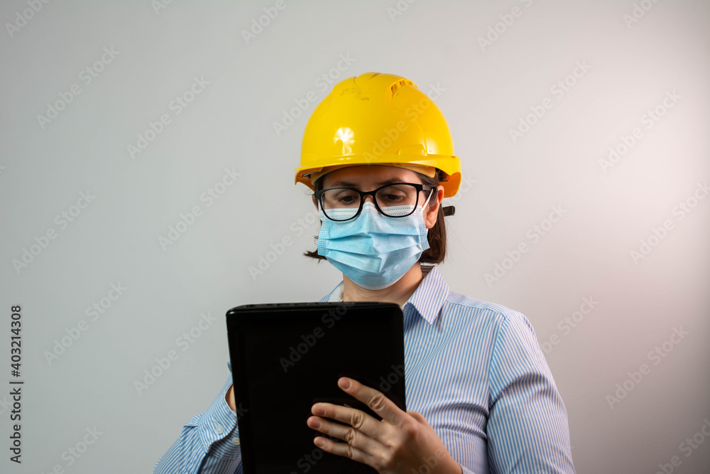 Female engineer using digital tablet while having conference call and wearing protective face mask due to coronavirus pandemic. Female engineer using digital tablet while having conference call and wearing protective face mask due to coronavirus pandemic.