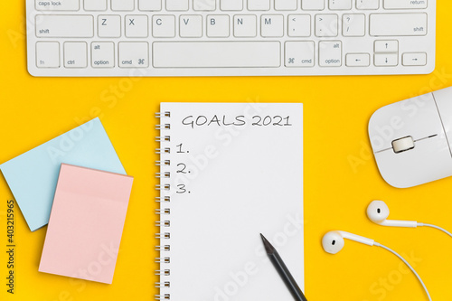 Text 2021 goals on notebook with pencil and office accessories on yellow background, office desk. Top view with copy space for input the text. 