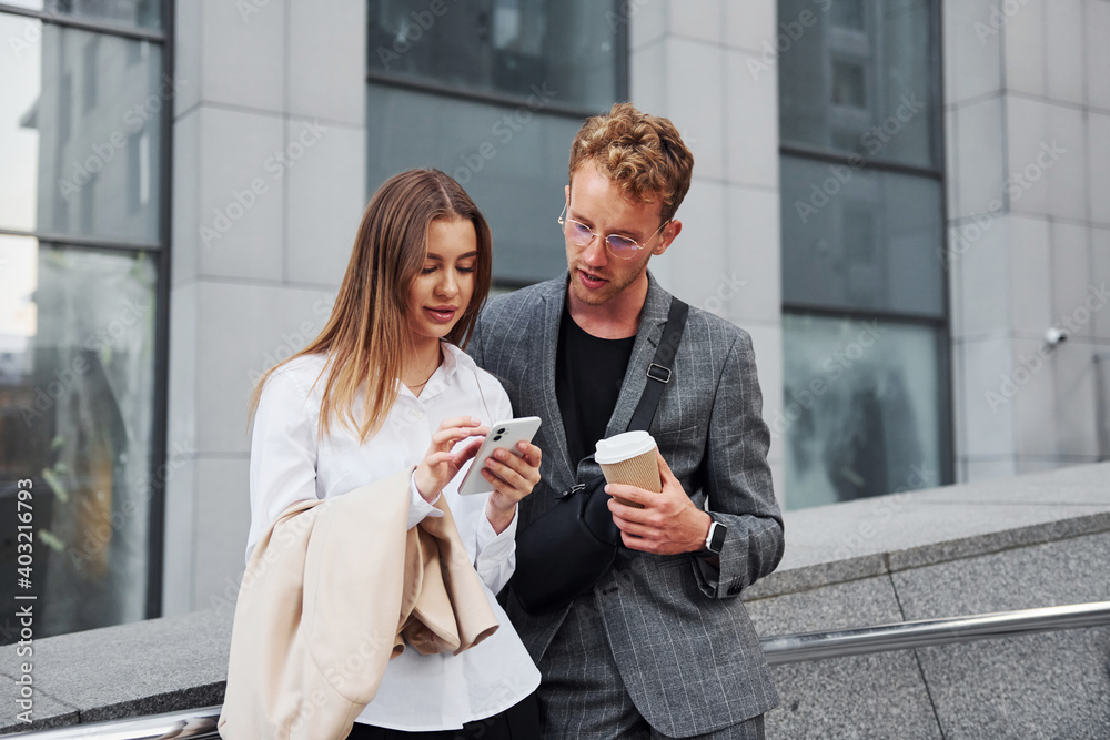 With phone and drink. Woman and man in the town at daytime. Well dressed people With phone and drink. Woman and man in the town at daytime. Well dressed people