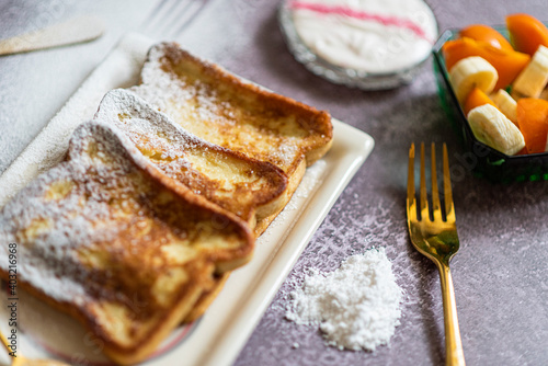 Traditional french toast with cinnamon on a gray background. Traditional Spanish sweet fried toasts  torrijas  with banana and persimmon  fresh cream  powdered sugar on a ceramic plate  and gold