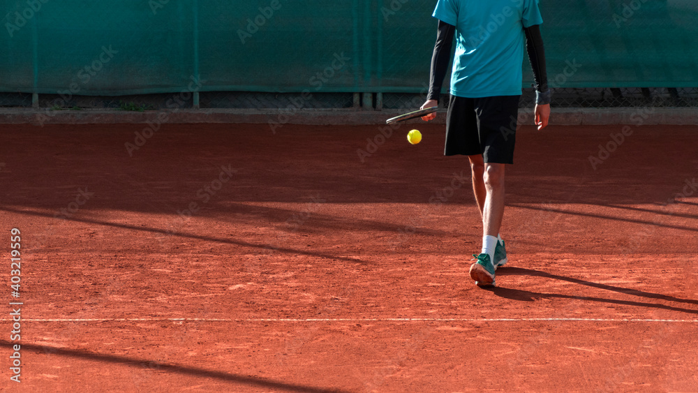Tennis player on red clay tennis court prepares to serve. Athlete with tennis racket and ball. Start of match, game, set. Sports panoramic background or banner with copy space.