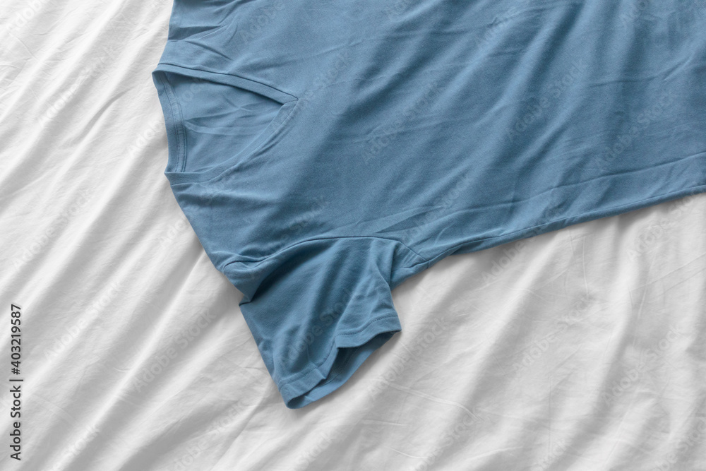 Blue simple t-shirt lie on white bed sheet. Blue simple t-shirt lie on white bed sheet.