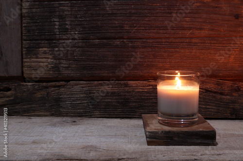 the burning luxury aromatic scented candle glass on the wooden table with background of vintage wooden wall of the cottage in the living room to creat relax ambient during christmas party celebration  photo