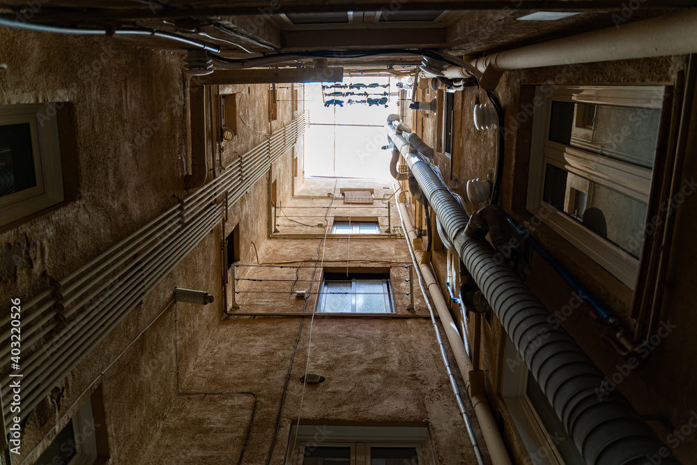 Fototapeta premium Well in courtyard of old buildings with windows, pipes and daylight