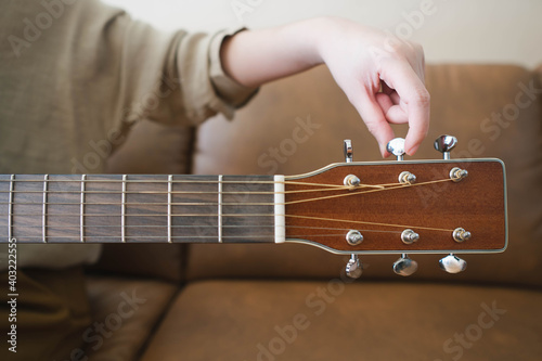 Woman hands tuning acoustic guitar strings before playing music lesson at home. Close up. photo