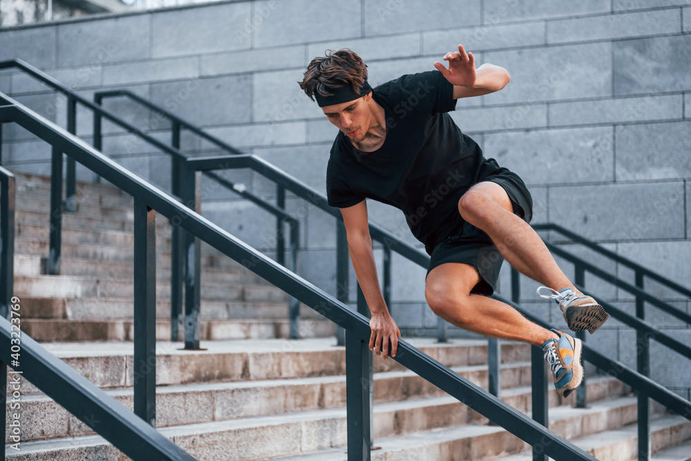 Fototapeta premium Jumps over obstacles. Young man in sportive clothes have workout outdoors at daytime