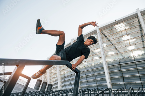 Does parkour. Young man in sportive clothes have workout outdoors at daytime