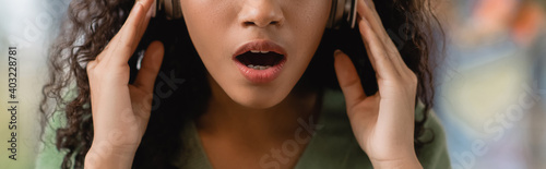 partial view of shocked african american woman listening podcast in cafe  banner
