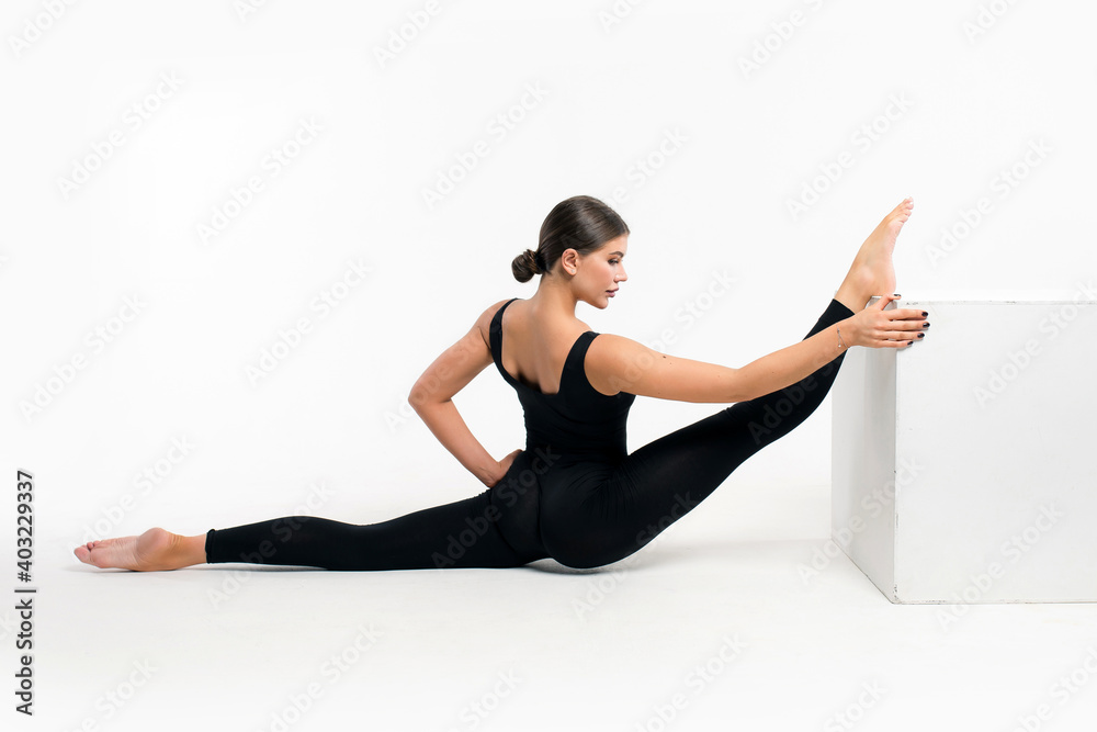 Flexible athletic woman in sportswear doing splits in fitness studio on  white background. Stretching exercises with a cube Stock Photo