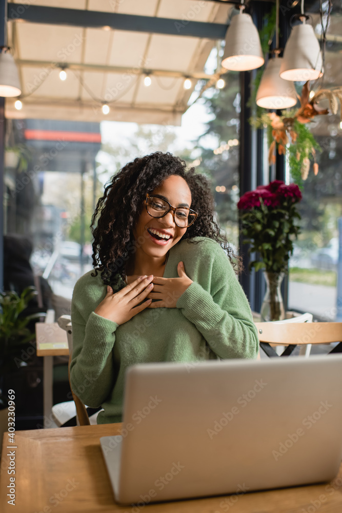 flattered african american woman in glasses looking at laptop on blurred foreground flattered african american woman in glasses looking at laptop on blurred foreground