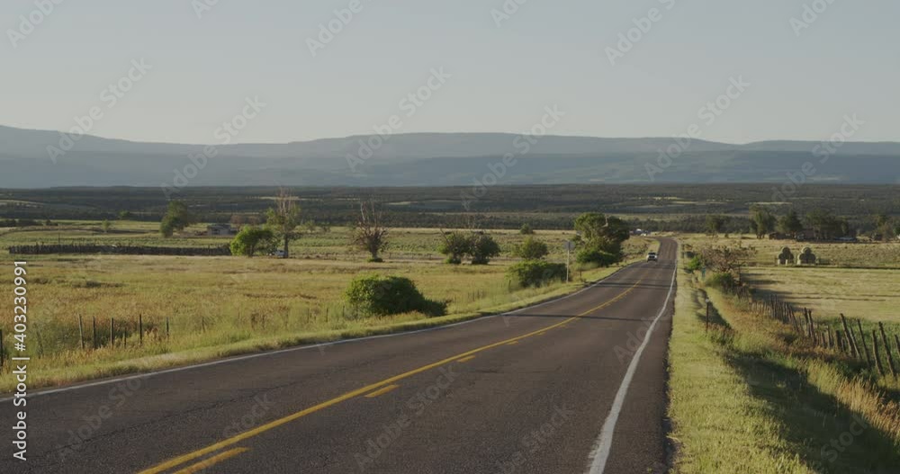 Straight asphalt road in Colorado flats, car approaching, mountains in background Straight asphalt road in Colorado flats, car approaching, mountains in background