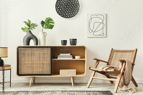 Stylish scandinavian living room interior of modern apartment with wooden commode, design armchair, carpet, leaf in vase, table lamp and personal accessories in unique home decor. Template. photo