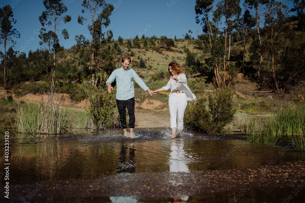 Fototapeta premium Couple running through the water, splashing each other. Welcoming the spring. Springtime