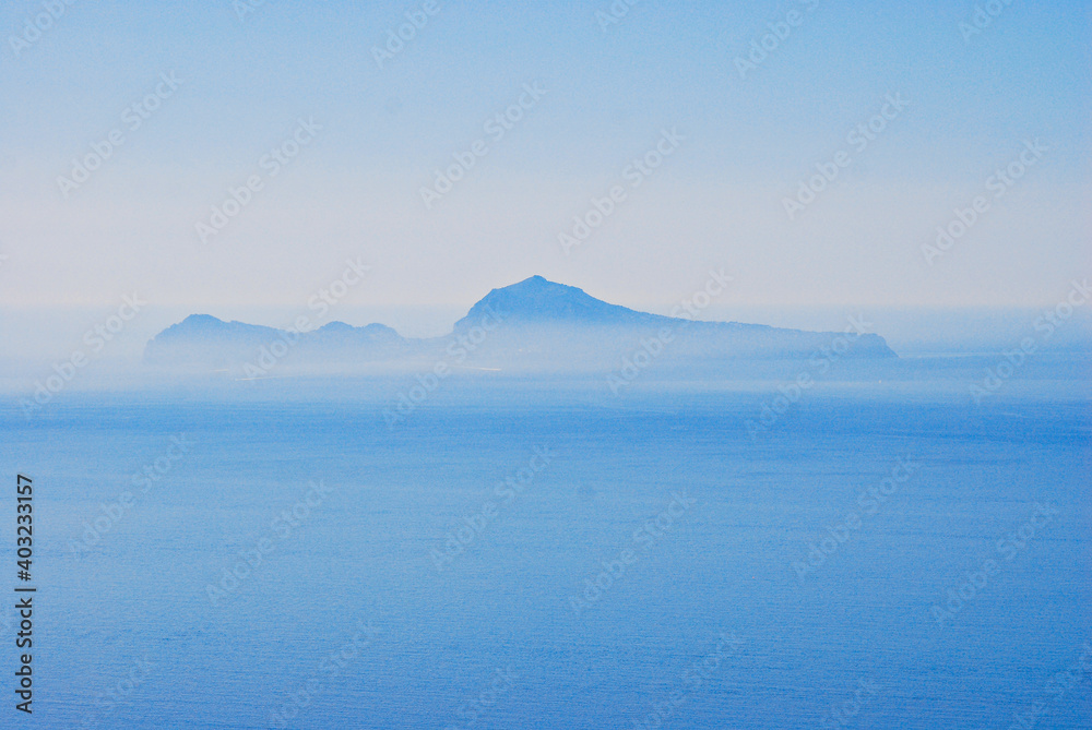 The Capri Island view from the Napoli Gulf in the lightblue mornings fog in south Italy