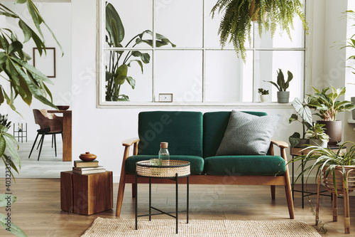 Stylish scandinavian living room interior with green velvet sofa, coffee table, carpet, plants, furniture, elegant accessories in modern home decor. Template.