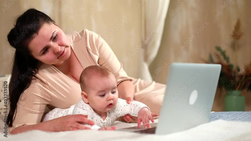 Young happy mother with baby girl using laptop resting on bed at home connecting with family online. Internet communicating. Freelance business. Social networking. Family chat. Female child uses tech. Young happy mother with baby girl using laptop resting on bed at home connecting with family online. Internet communicating. Freelance business. Social networking. Family chat. Female child uses tech.