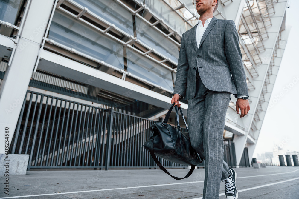 © standret - Walks on the road. Young businessman in grey formal wear is outdoors in the city